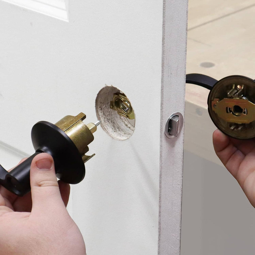 Hands installing a door lock cylinder on a drilled door face with matching plate