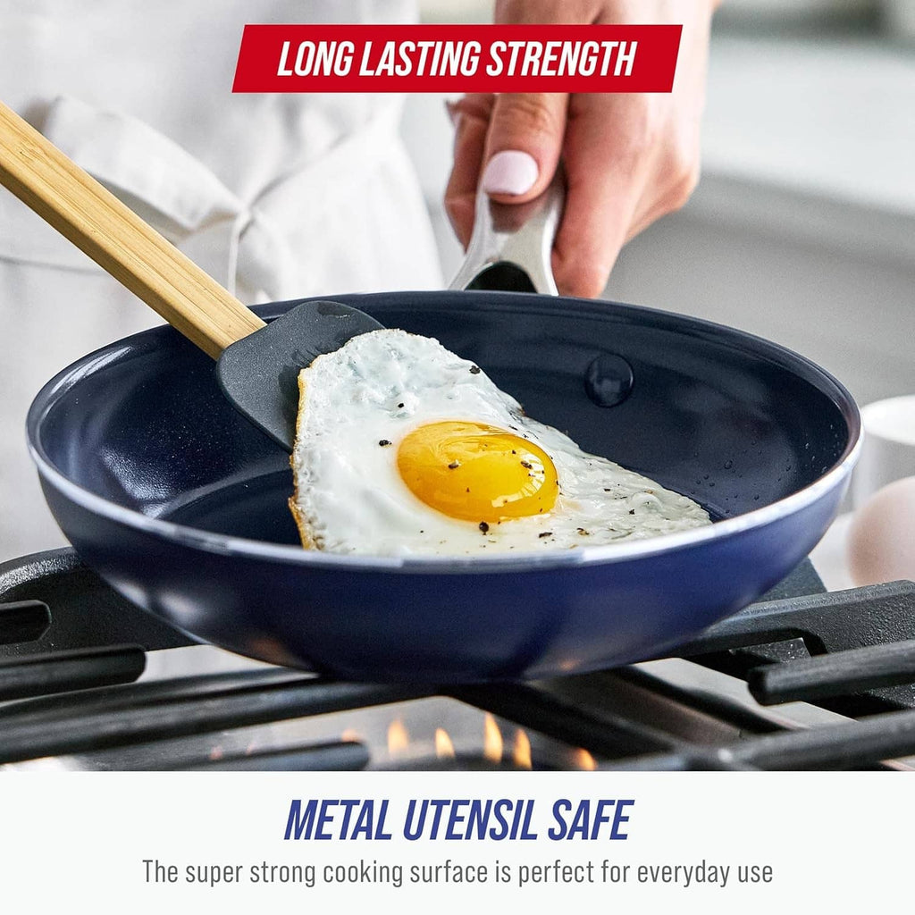 Blue ceramic nonstick frying pan on a stovetop with spatula and fried egg