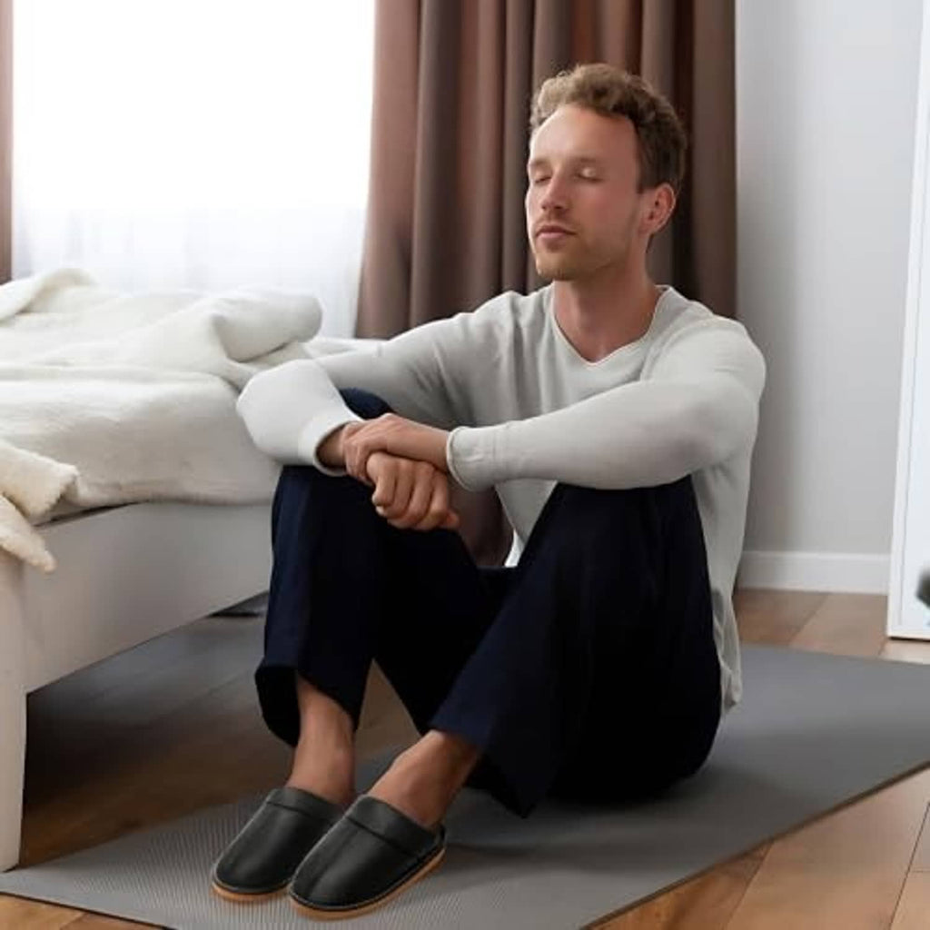 Man wearing black leather slip-on slippers with fuzzy lining and tan sole