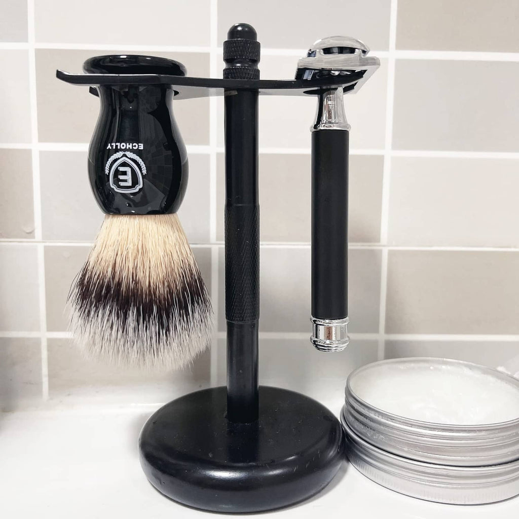 Men's black shaving brush on stand with dense bristles, near razor and shaving cream