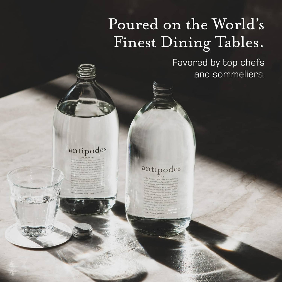 Two Antipodes sparkling artesian water bottles with two tumblers on tabletop