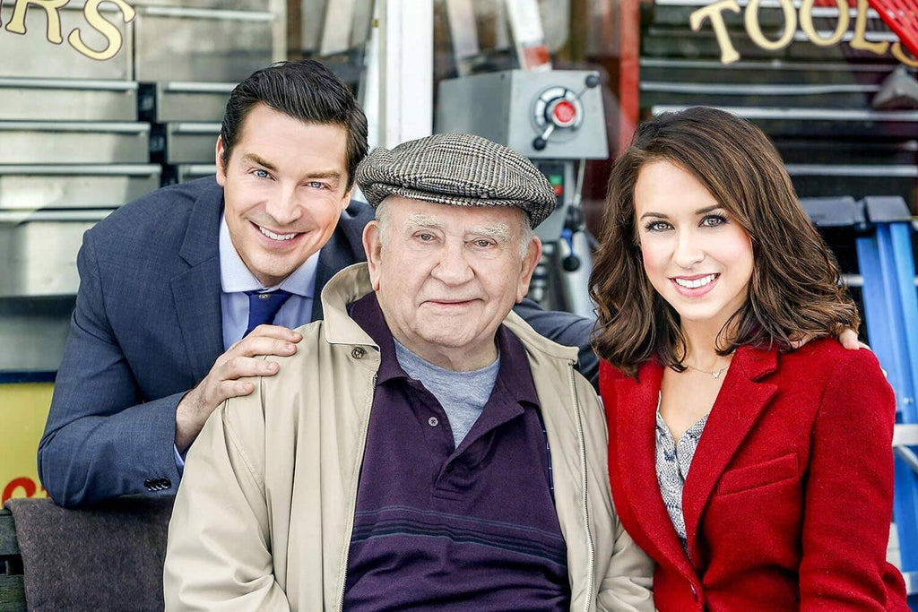 Film still of three smiling actors posing together, one in a cap and tan jacket