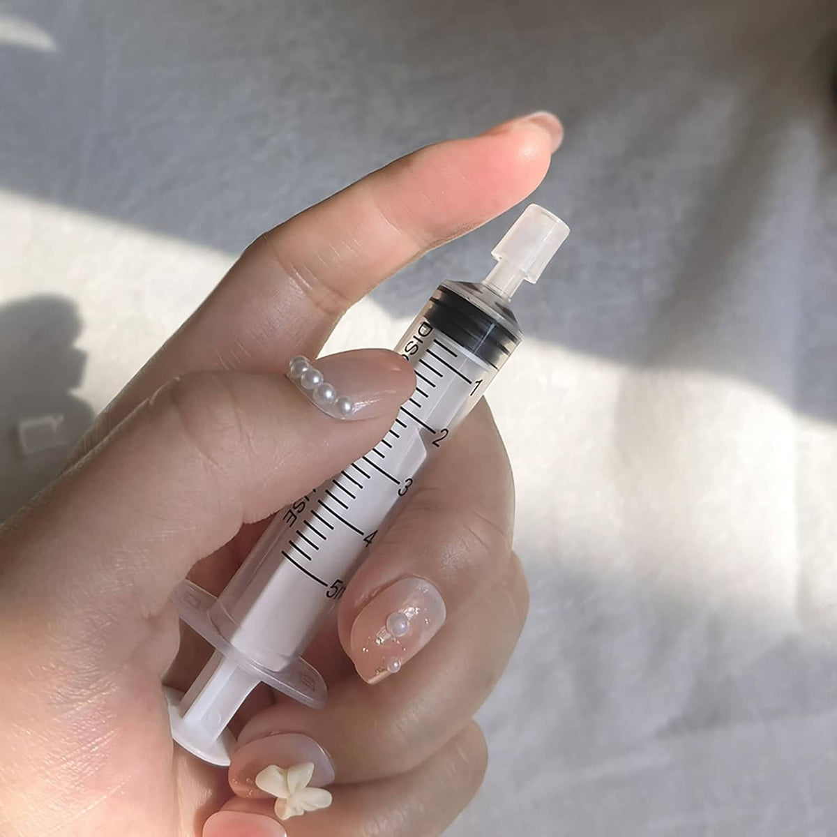 Hand holding clear measuring syringe with fine nozzle for perfume extraction
