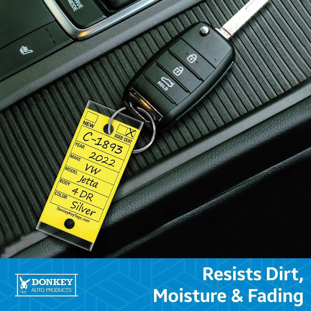 Laminated yellow key tag attached to a car key fob on textured dashboard surface