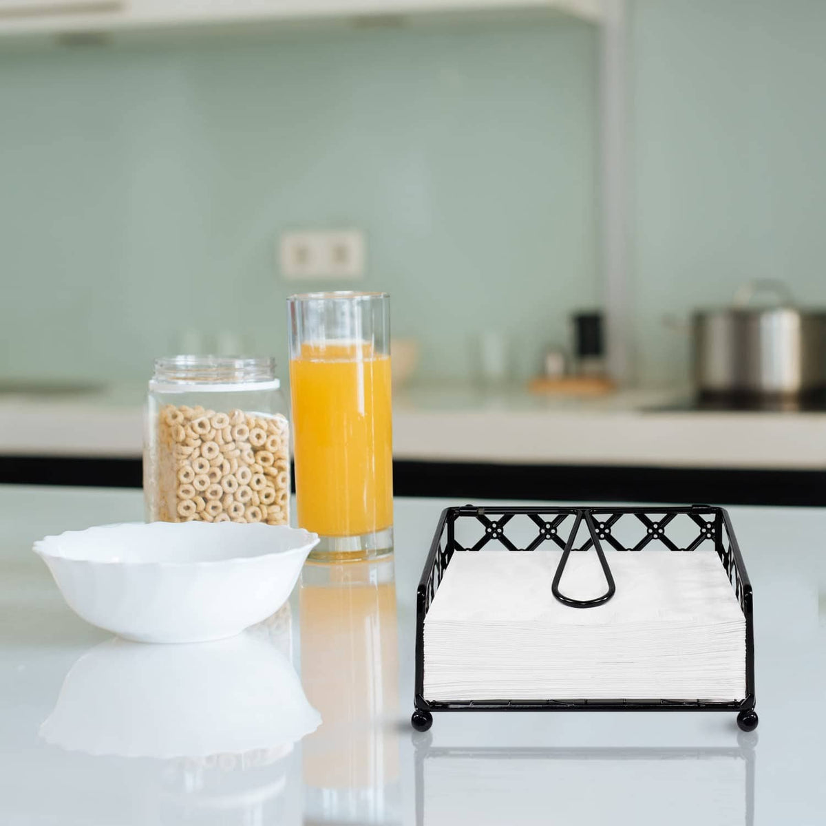 Black lattice napkin holder with white napkins and curved handle, on counter.