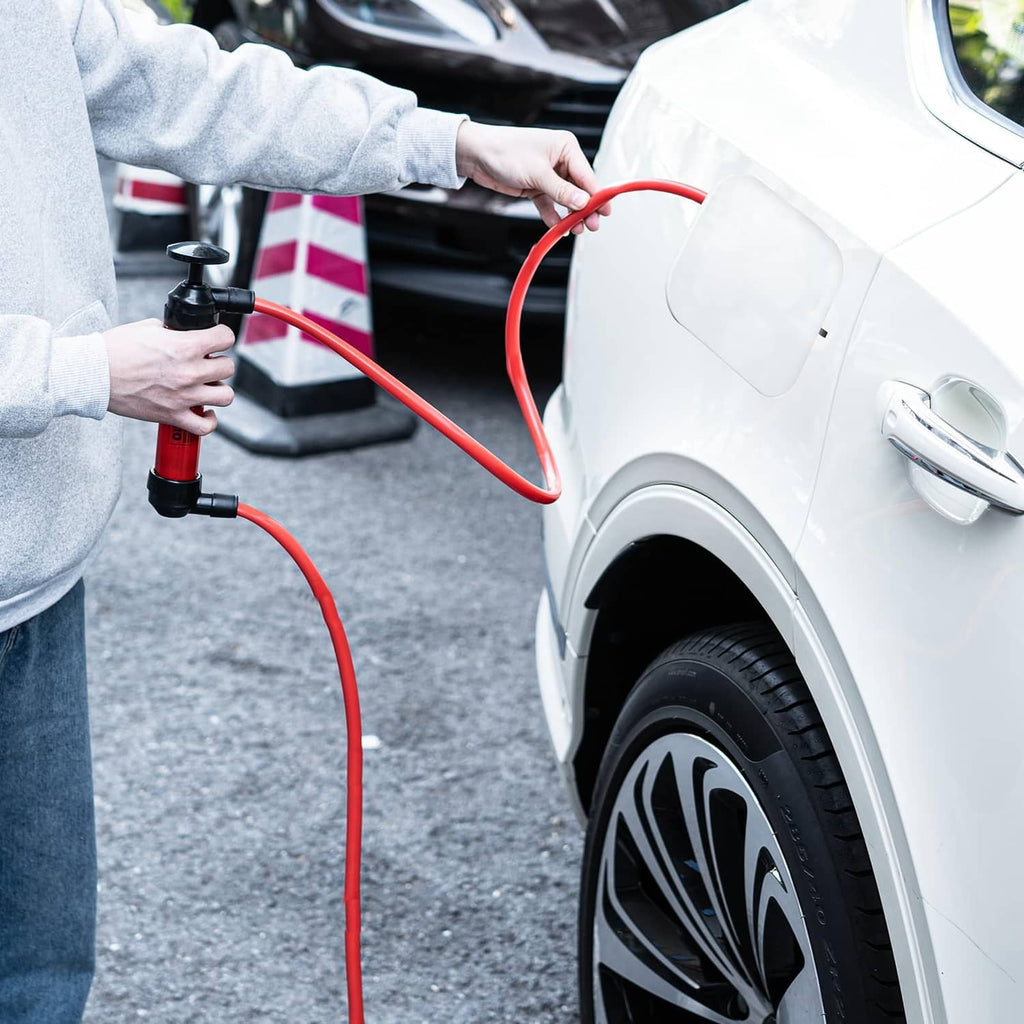 Hand siphon pump dispensing fuel via red hose, with black pump head and connectors