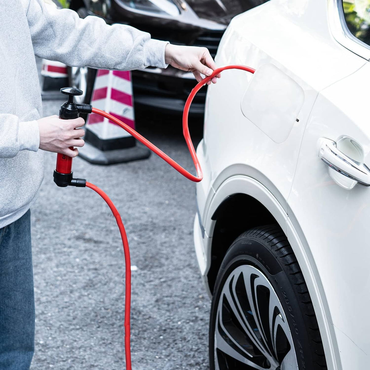 Hand siphon pump dispensing fuel via red hose, with black pump head and connectors