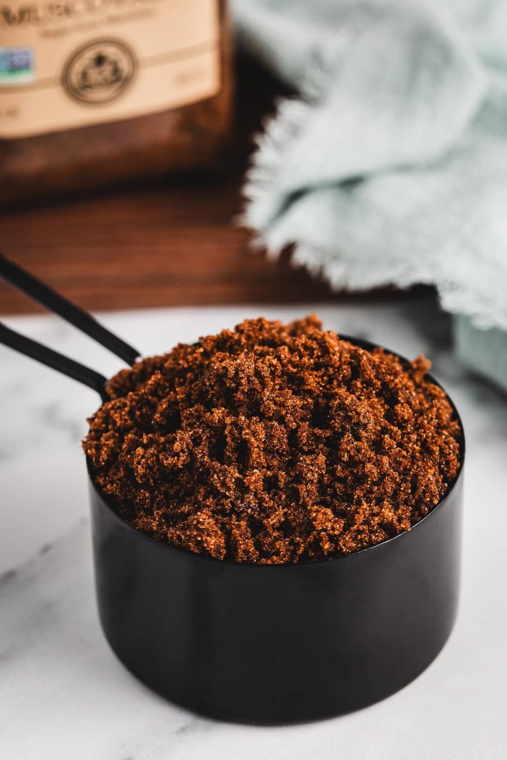Dark muscovado sugar granules in black measuring cup