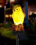 Yellow glowing owl solar garden stake light with log base and black solar panel