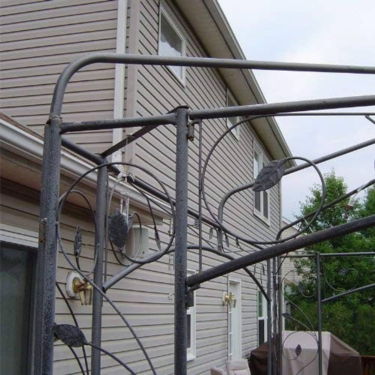 Gazebo canopy top cover secured to metal frame with support bars near house siding