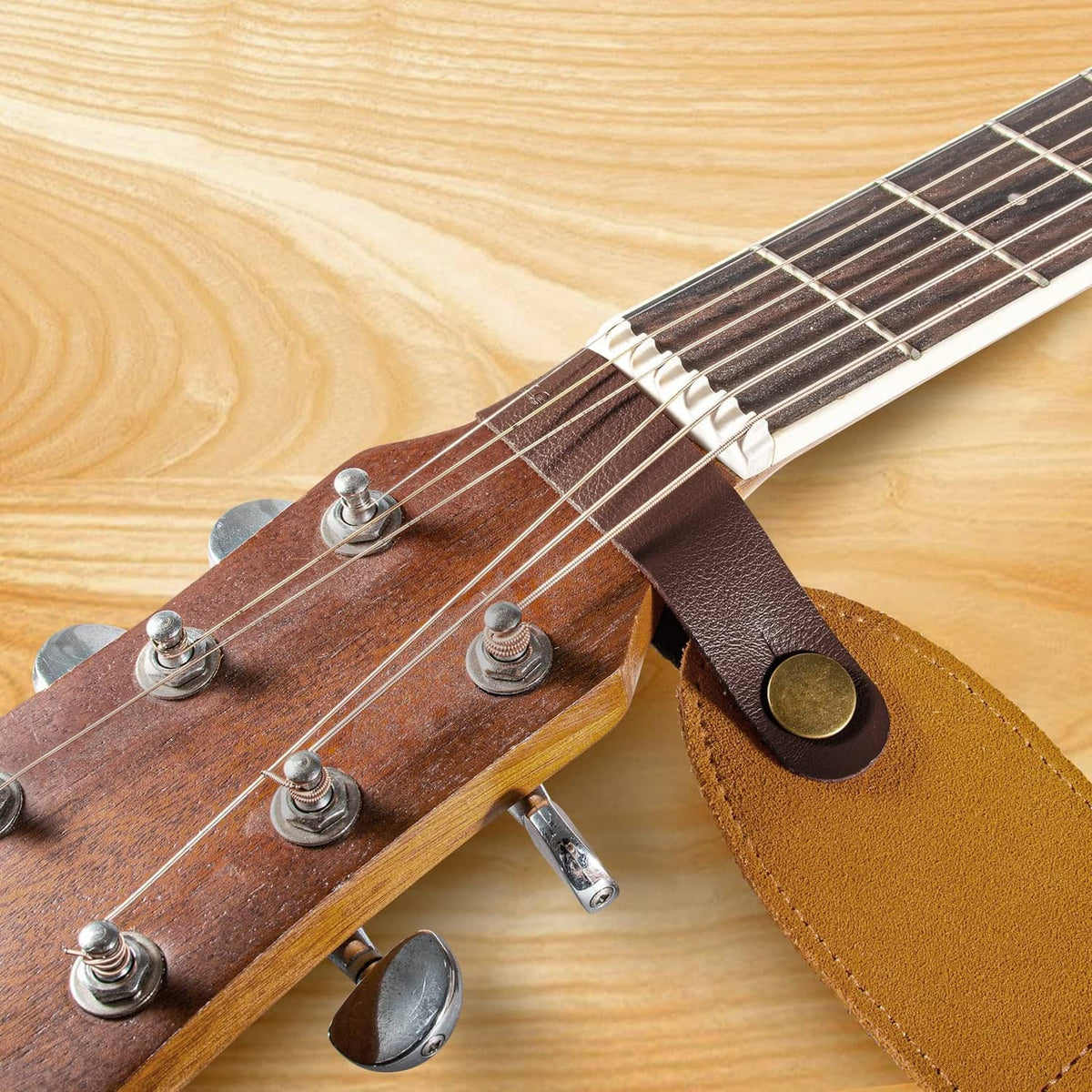 Leather guitar headstock strap adapter tied to headstock with tan strap and brass button