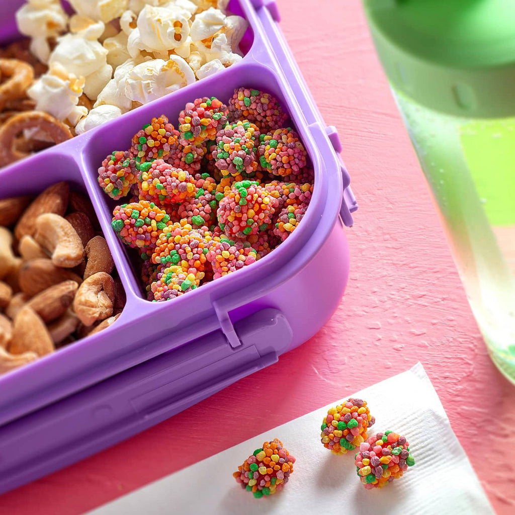 Purple container filled with rainbow gummy clusters with a few pieces on paper