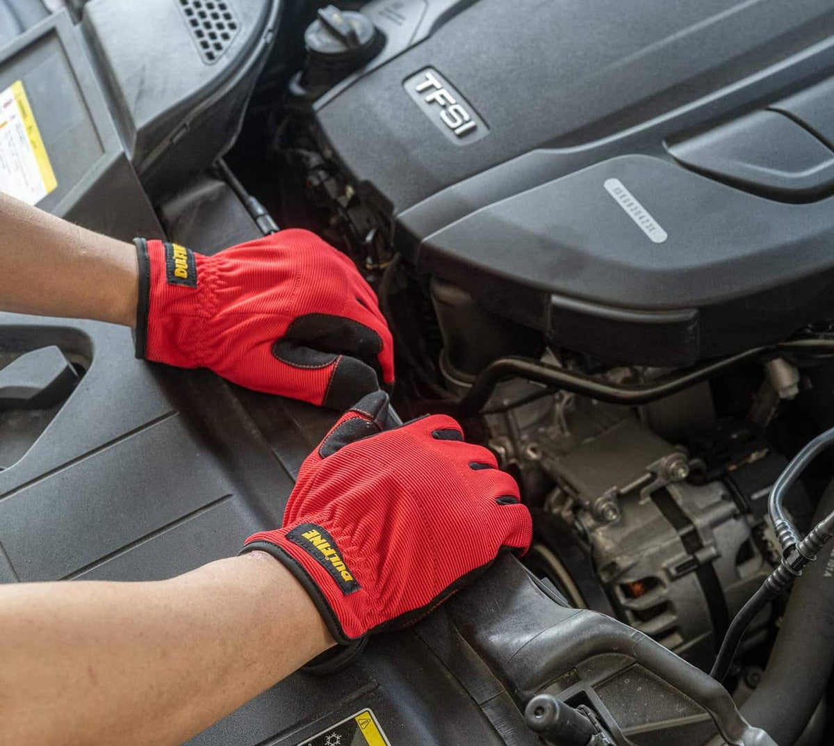 Red and black work gloves worn on hands gripping a vehicle engine compartment