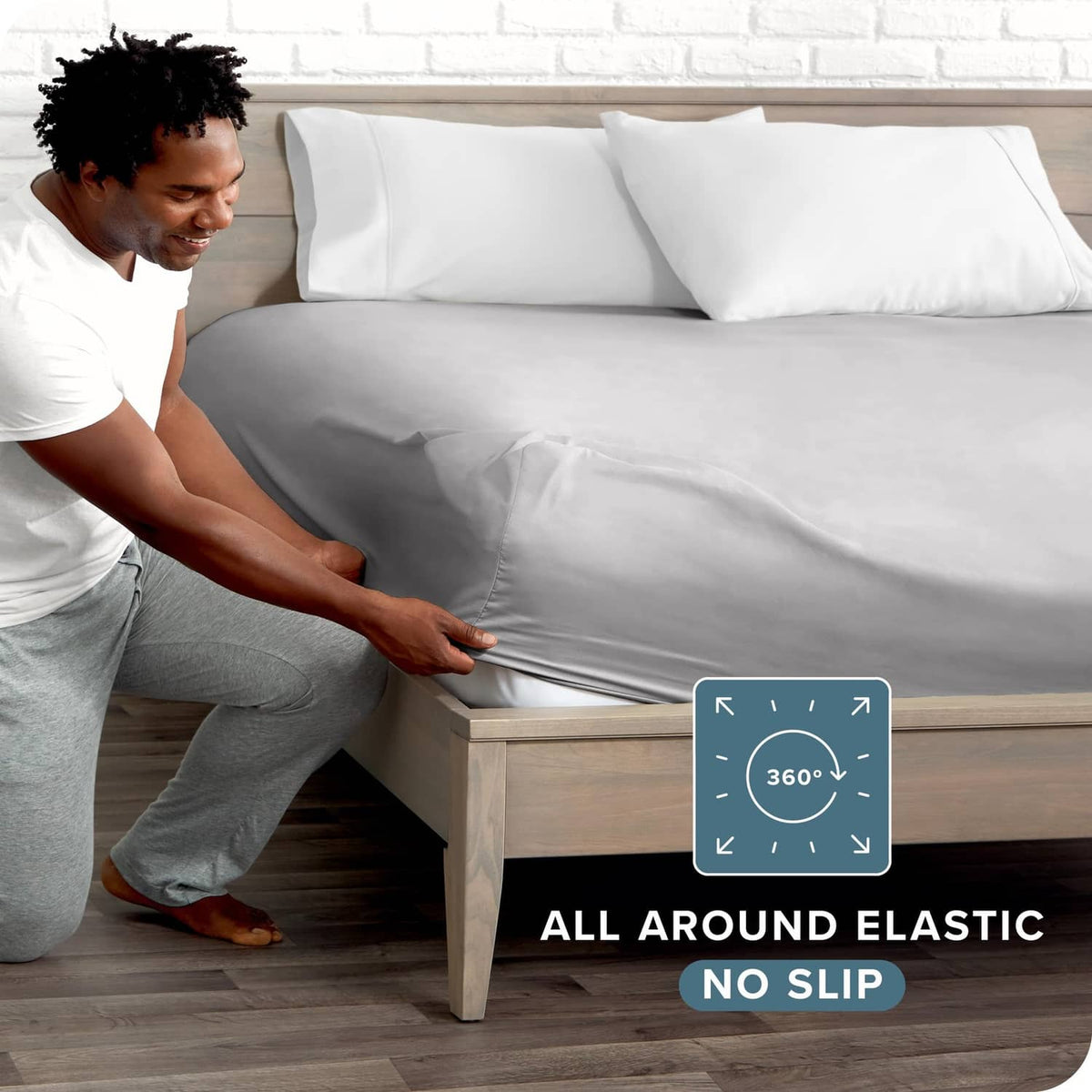 Light grey fitted sheet being stretched over bed frame, corner elastic visible