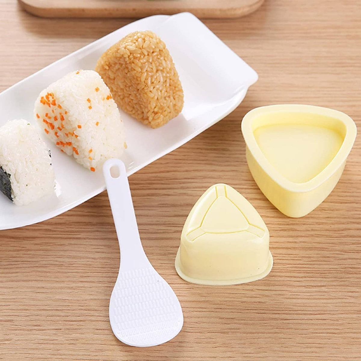 Onigiri triangle press molds with ridged white paddle, cream-yellow pieces on tray