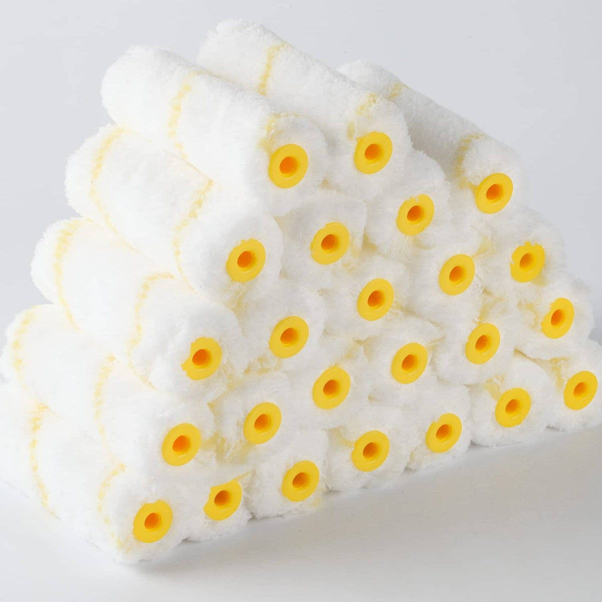 Close-up bundle of 4-inch paint roller covers with fluffy white nap and yellow cores