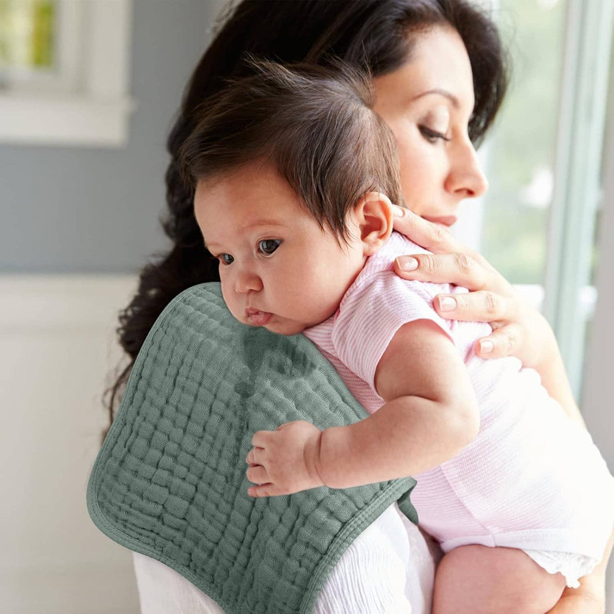 Muslin burp cloth in sage green, placed over baby as parent holds and comforts them