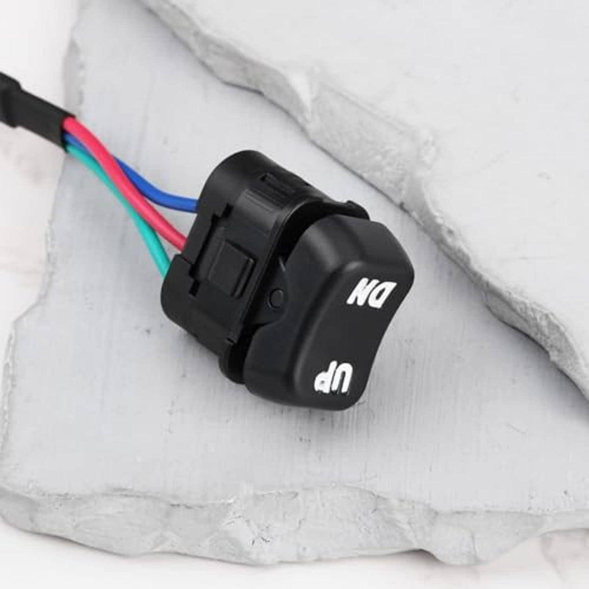 Black tilt/trim rocker switch with colored 3-wire leads on white stone surface