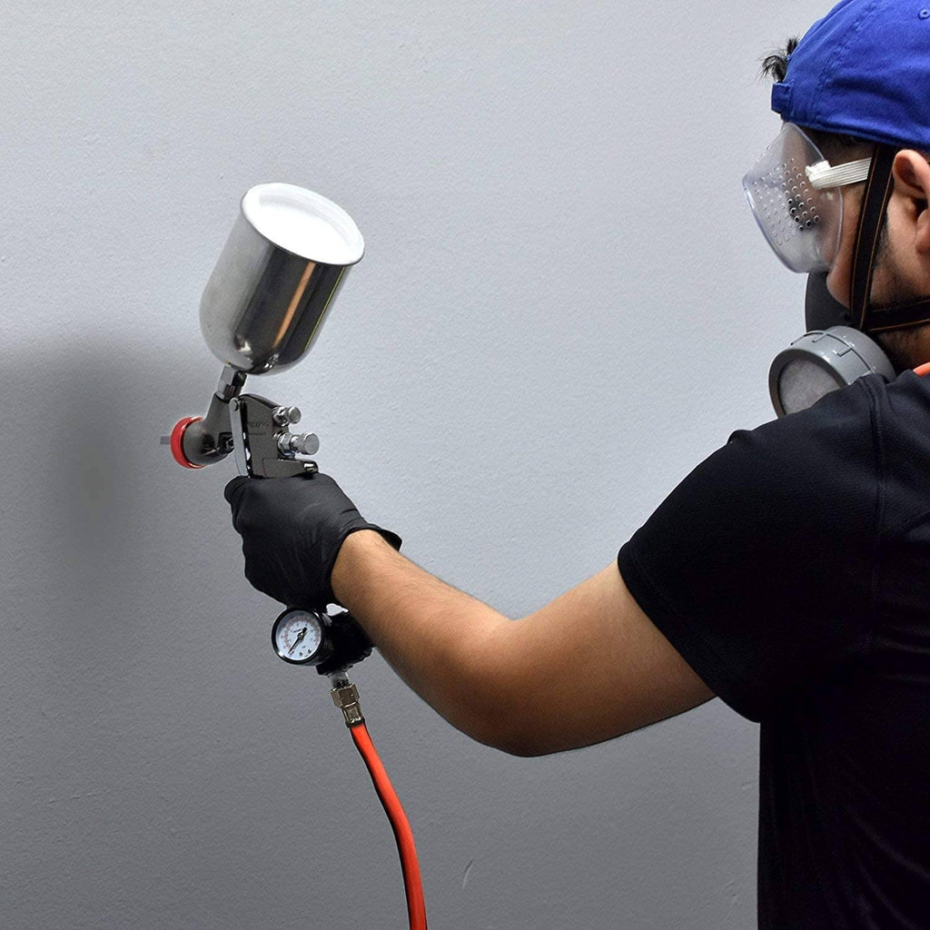 Painter using an air spray paint gun with gravity cup and red hose connector