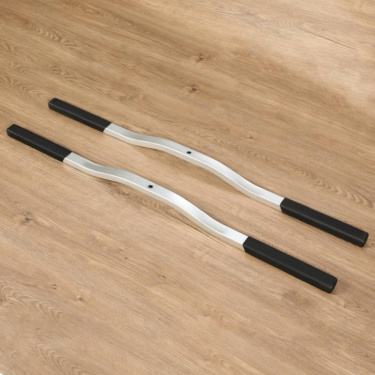 Two silver ski tie-down bars with black boots, spaced parallel on a flat surface