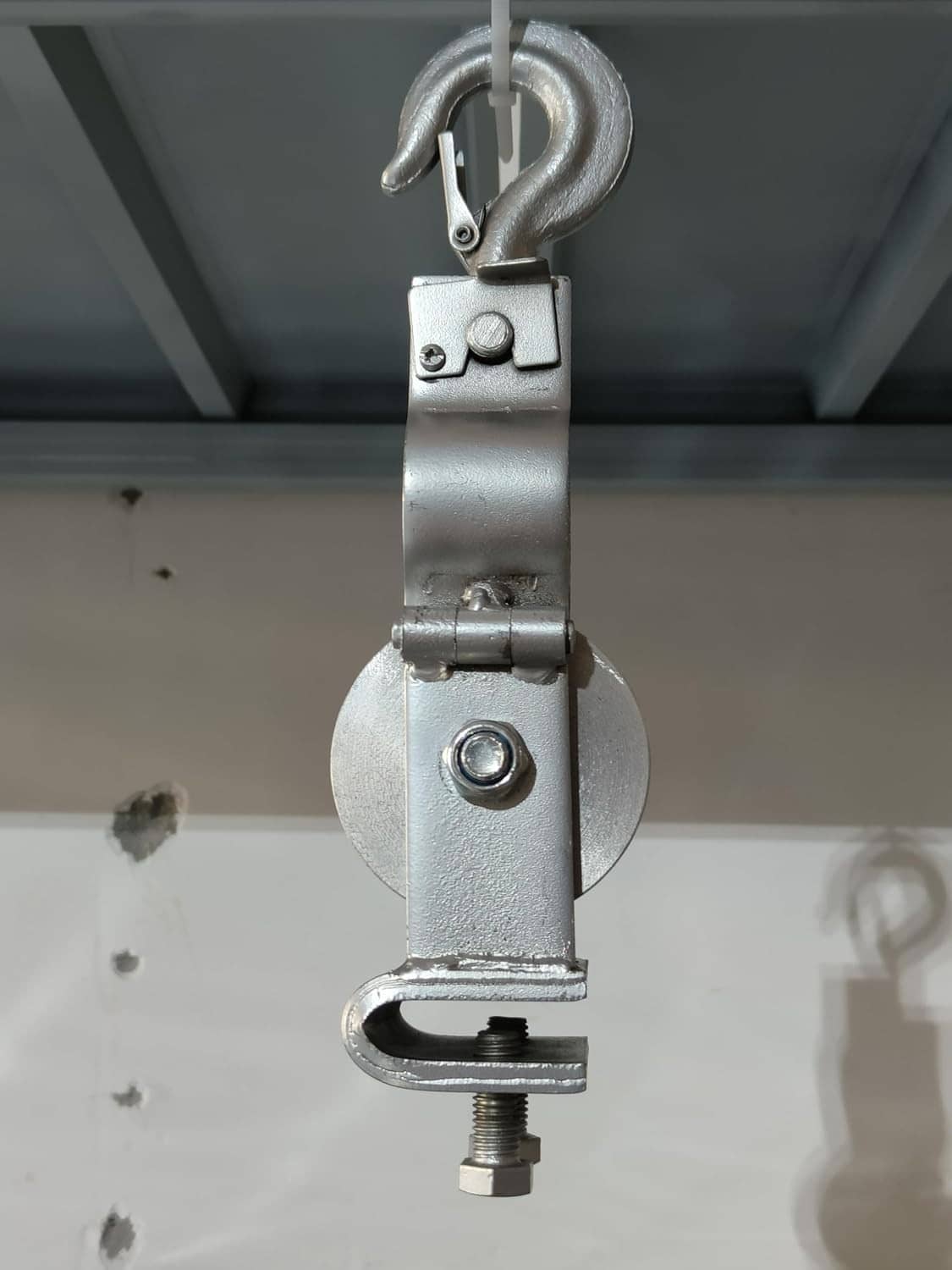 Cable pulley hook block mounted to a surface with cast sheave wheel and bolts