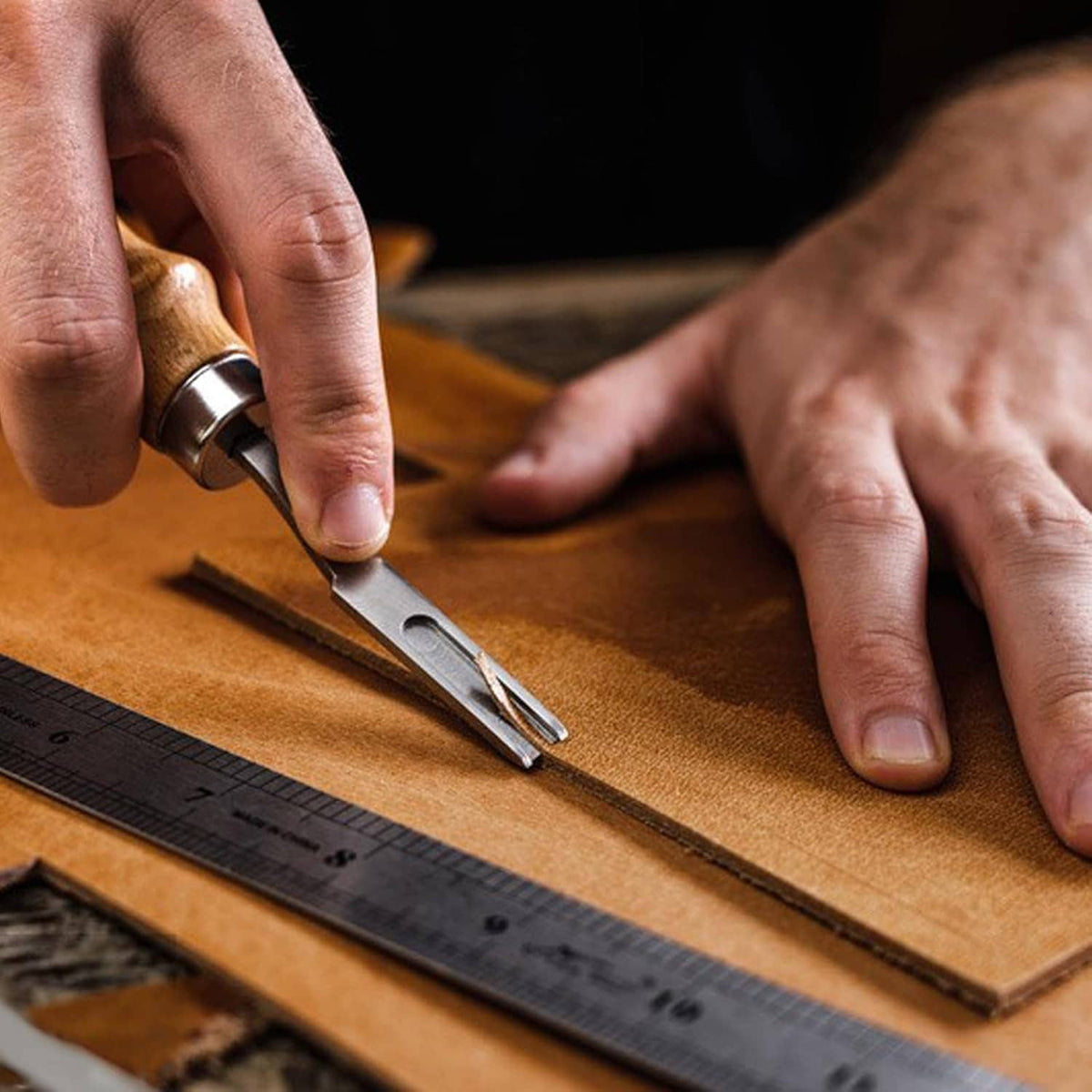 Hands cutting brown full grain leather sheet with a craft knife template.