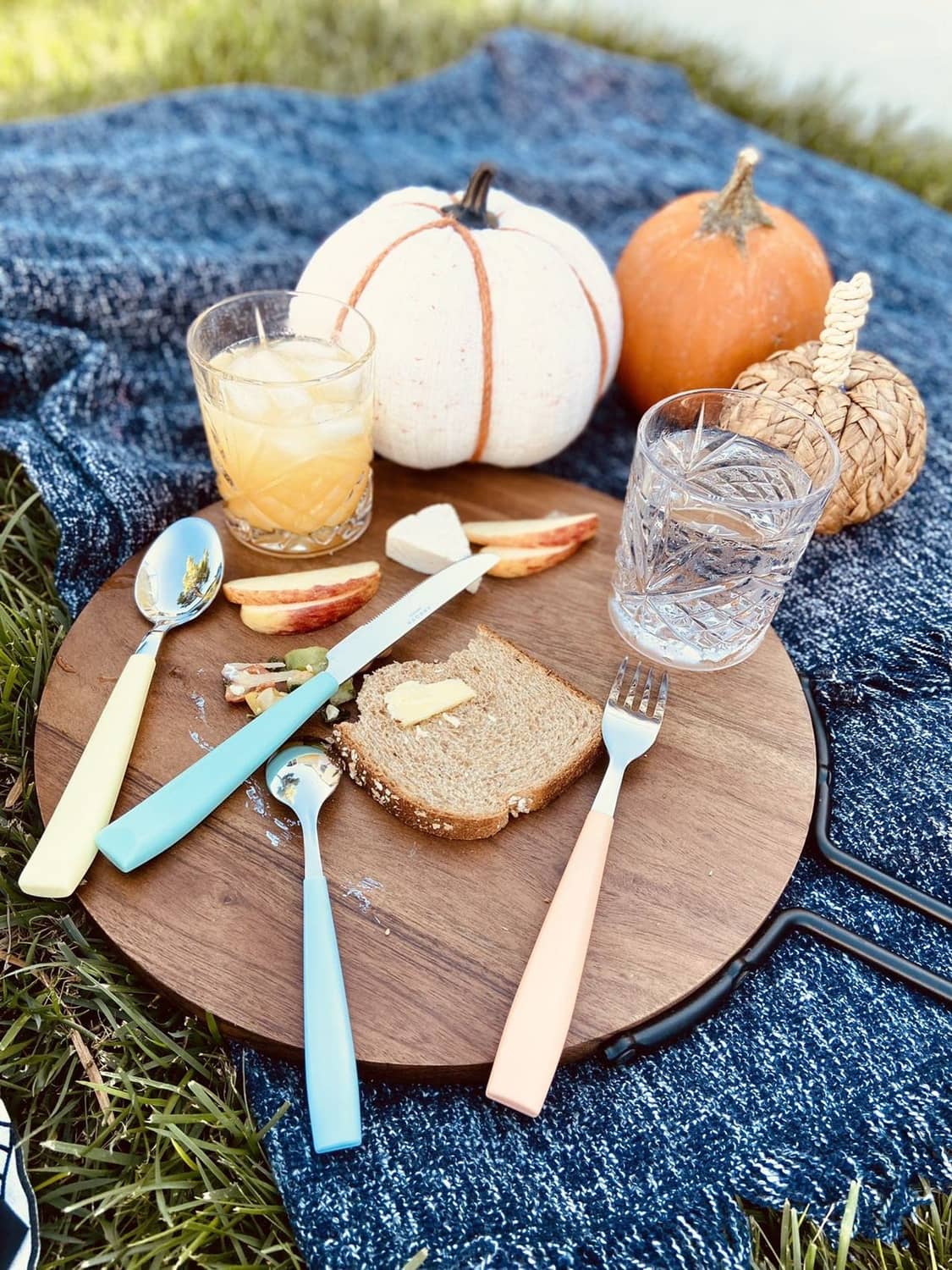Stainless steel cutlery with colorful handles resting on a wooden board with bread