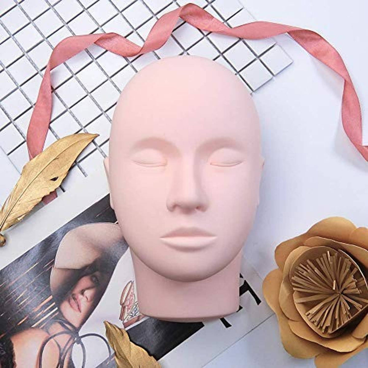 Beige lash training mannequin head with closed eyes and pink satin ribbon