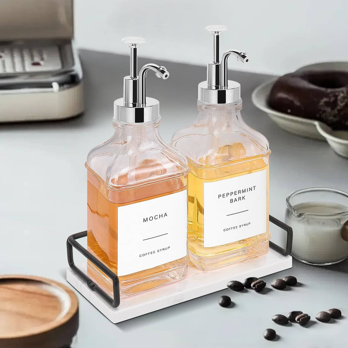 Two glass coffee syrup bottles with chrome pumps on marble-look tray, amber contents