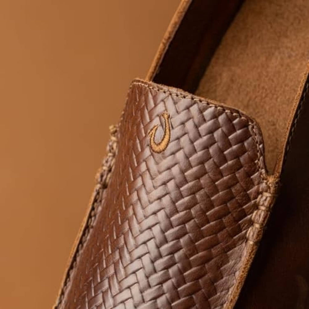 Close-up of woven leather slip-on toe with tan emblem and stitched edge