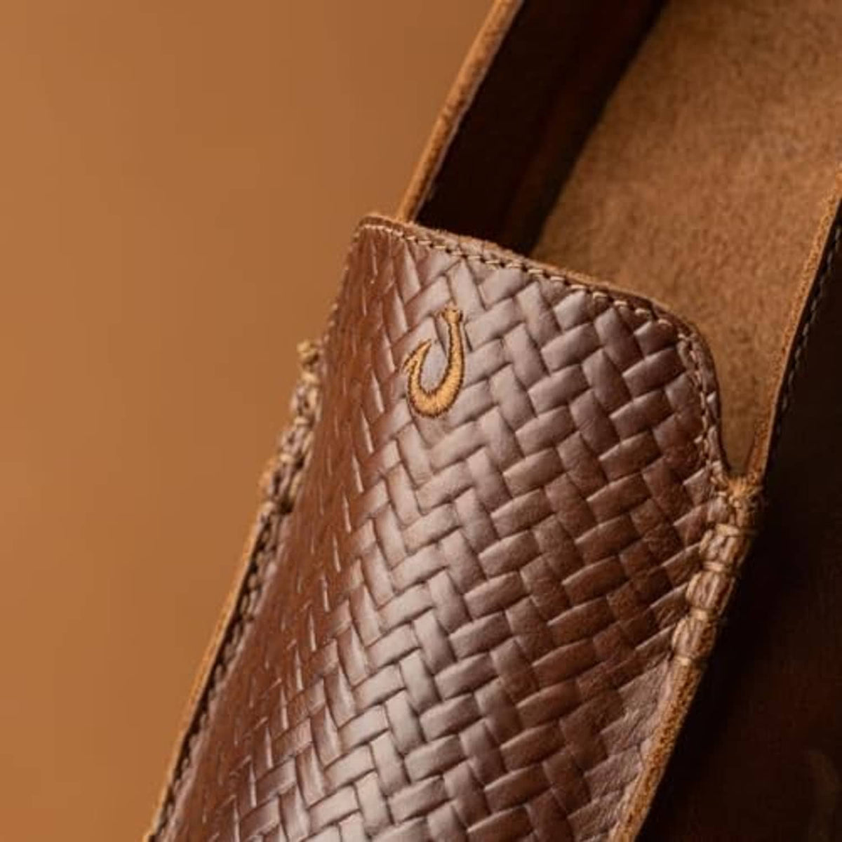 Close-up of woven leather slip-on toe with tan emblem and stitched edge