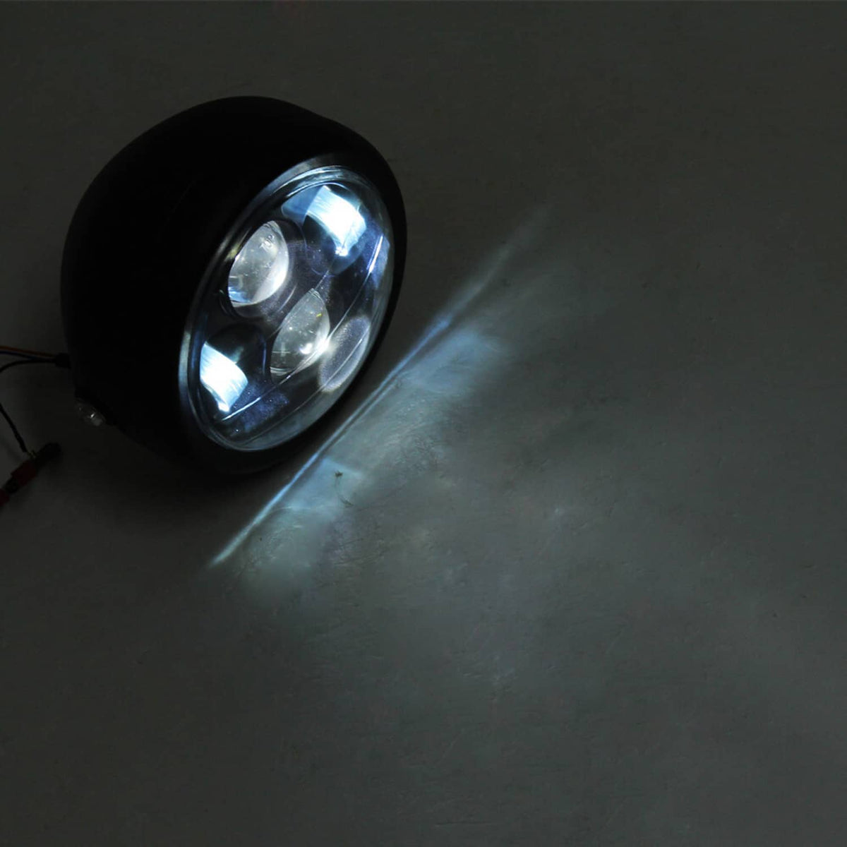Glowing round LED motorcycle headlight angled on a dark surface
