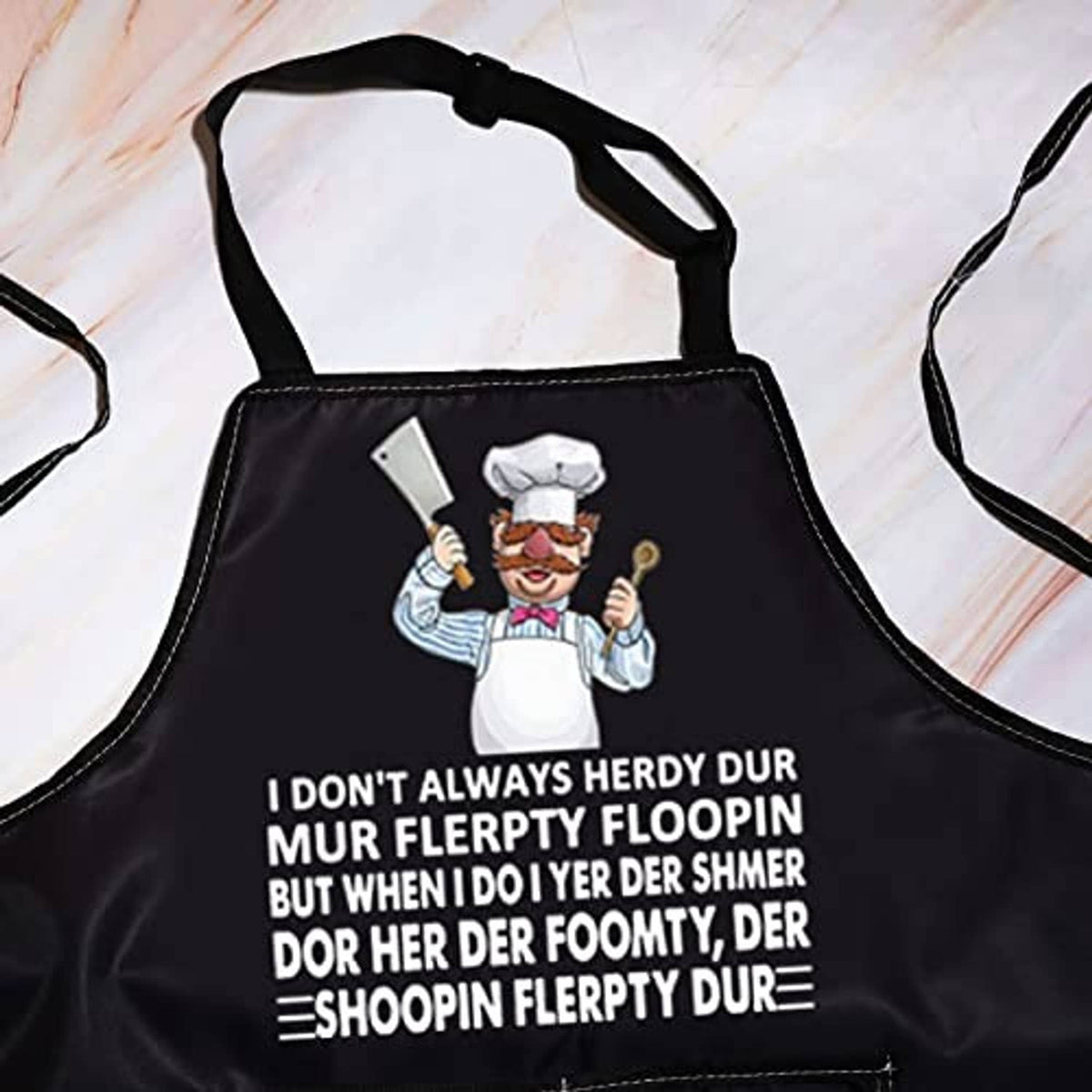 Black apron close-up with chef cartoon, printed slogan text, and visible front pocket.
