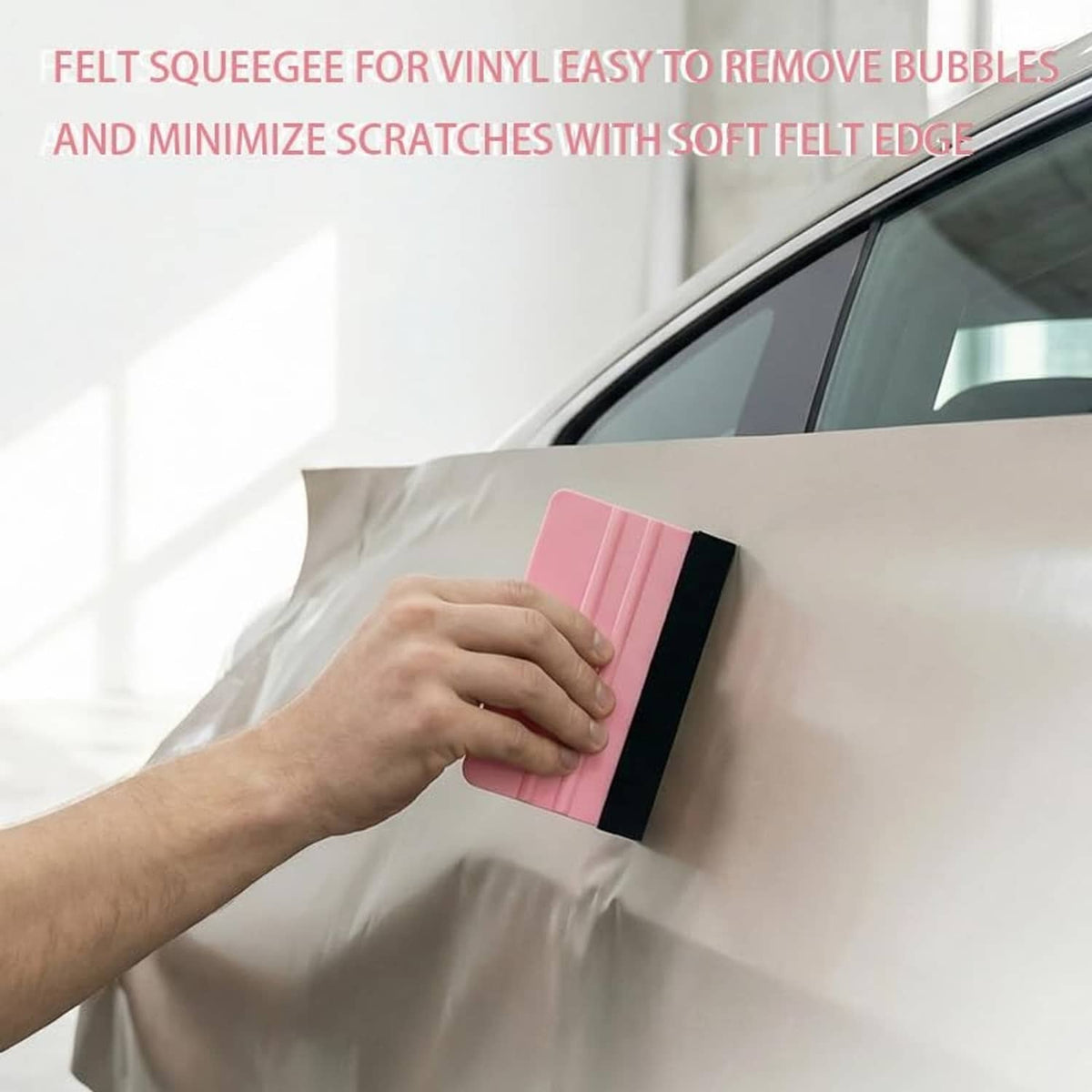 Hand using pink-and-black vinyl squeegee to smooth clear film on car window