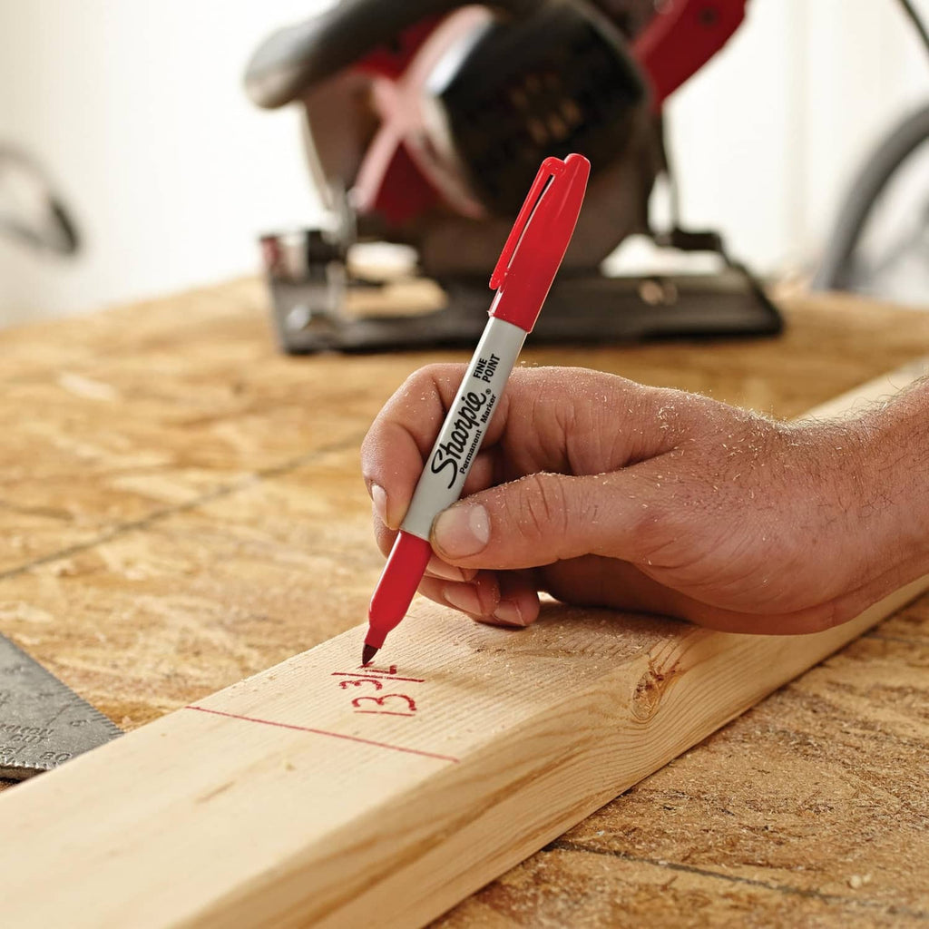 Red fine-point permanent marker held in a hand writing on a wooden board