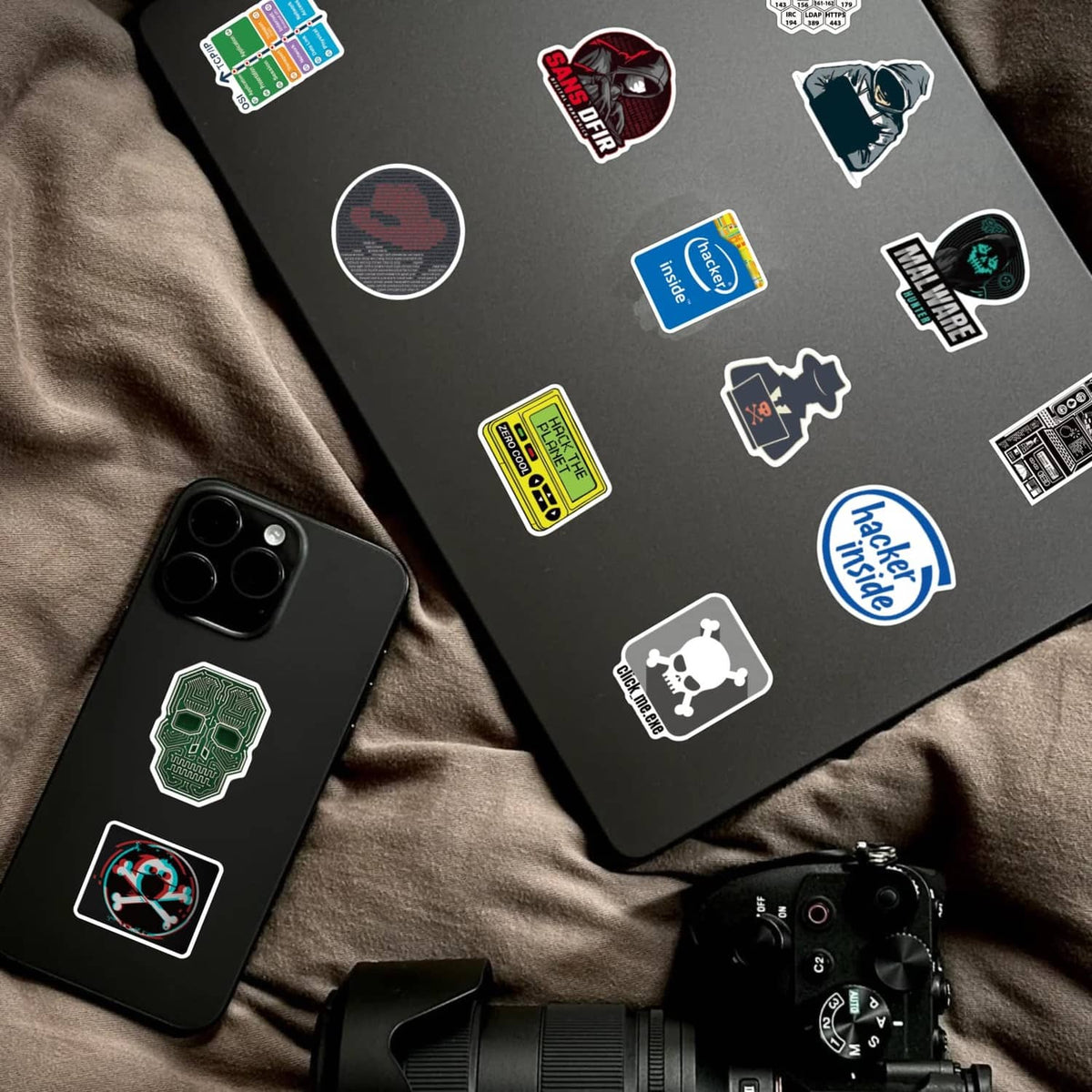 Hacker-themed stickers on a dark laptop and phone case with tech logos and badges