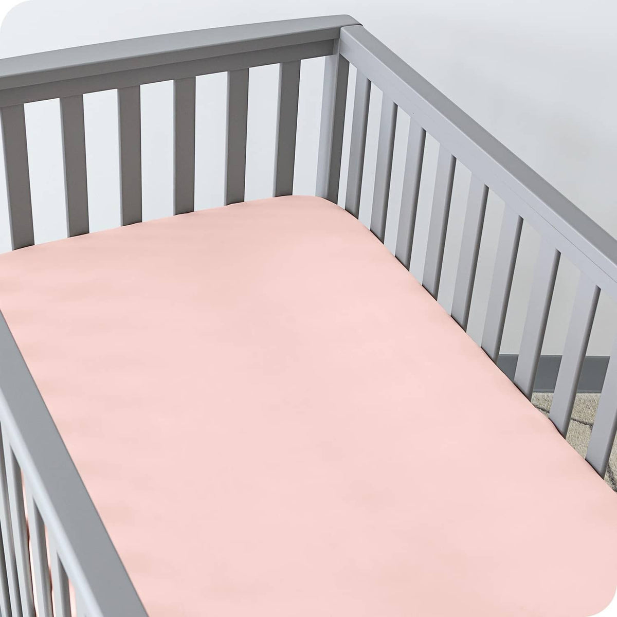 Pink crib fitted sheet laid flat on crib mattress, smooth top surface and corners