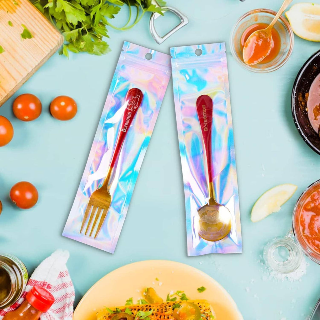 Two holographic mylar pen bags with hanging holes on a flat surface