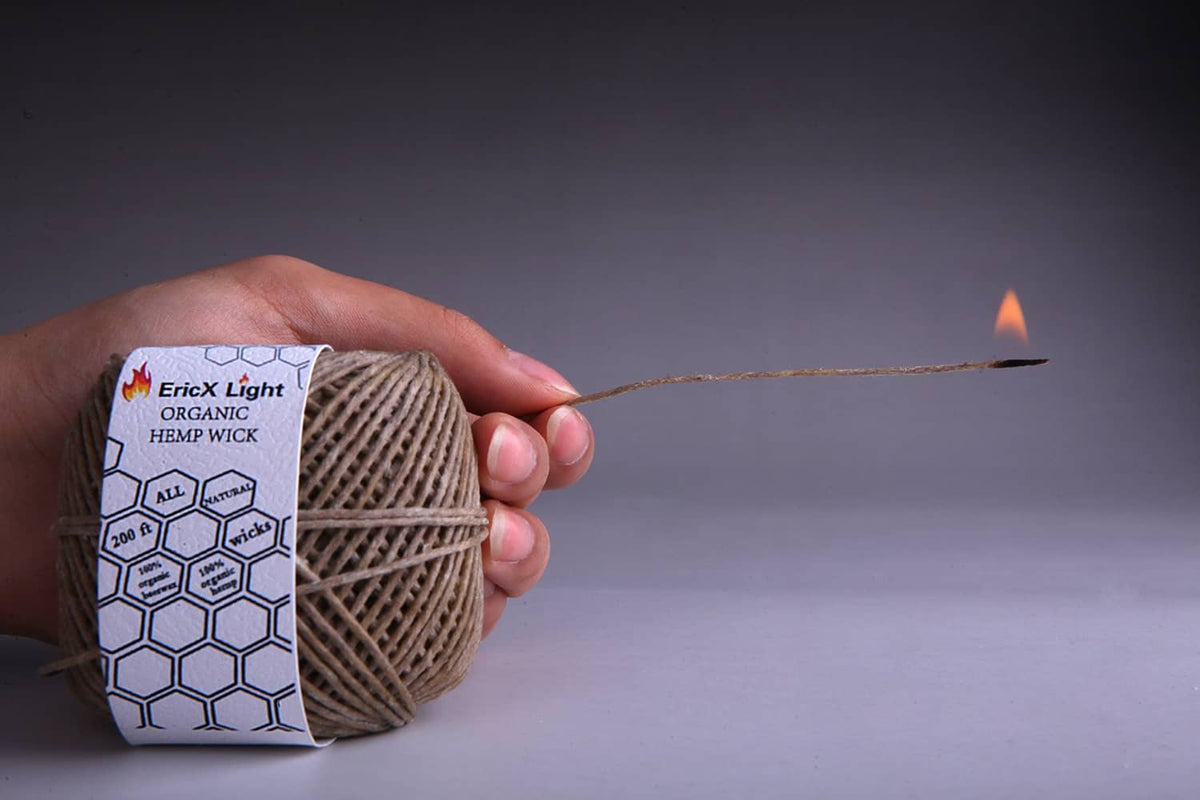 Hand holding organic hemp wick spool; wick end burning with small flame