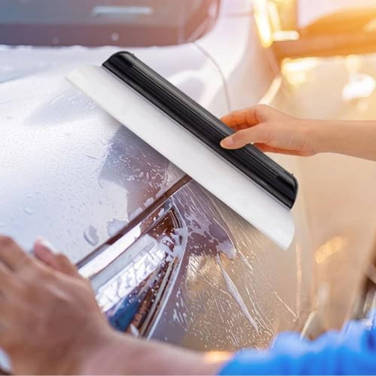 Hand using a black silicone car squeegee to remove water from windshield