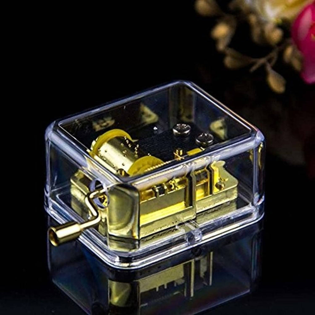 Close view of clear music box and gold hand-crank mechanism with side crank handle.