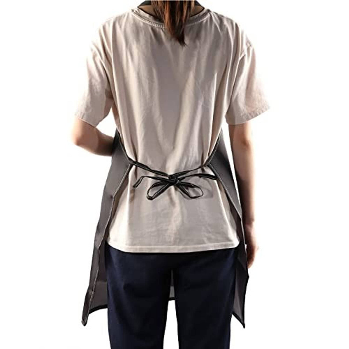 Black apron with waist tie and adjustable neck, worn over a light beige shirt.