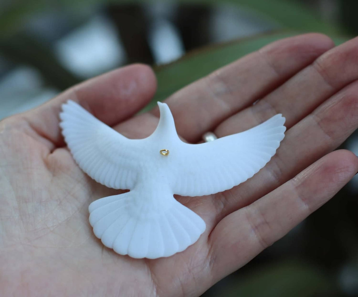 White dove ornament held in a hand, with small gold eye detail