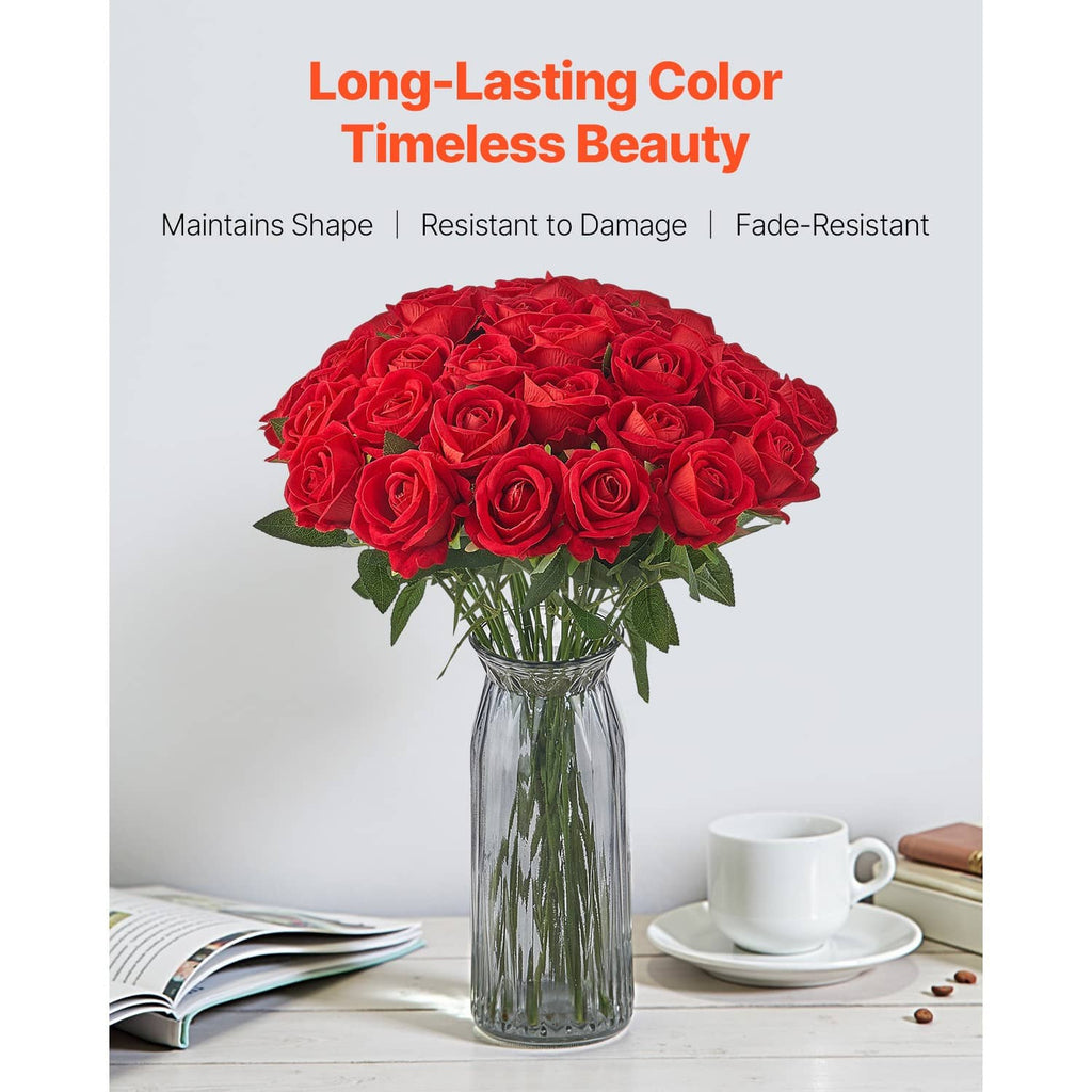 Red artificial rose bouquet in a glass vase with green leaves