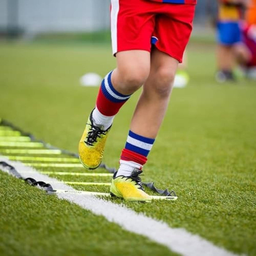 Agility ladder with bright yellow rungs and black straps on grass training field
