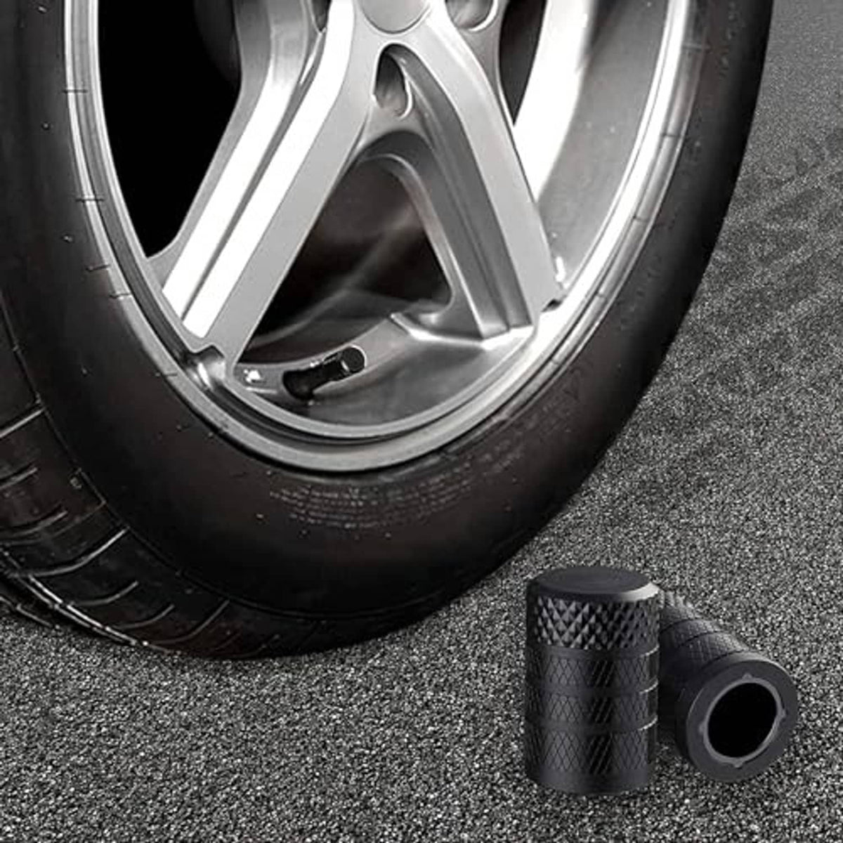 Black tire valve stem caps on gray pavement with car wheel in background, valve end visible