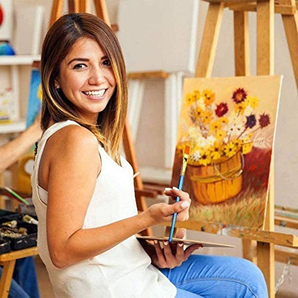 Paint brush with blue handle and gold ferrule in use, painting a small canvas
