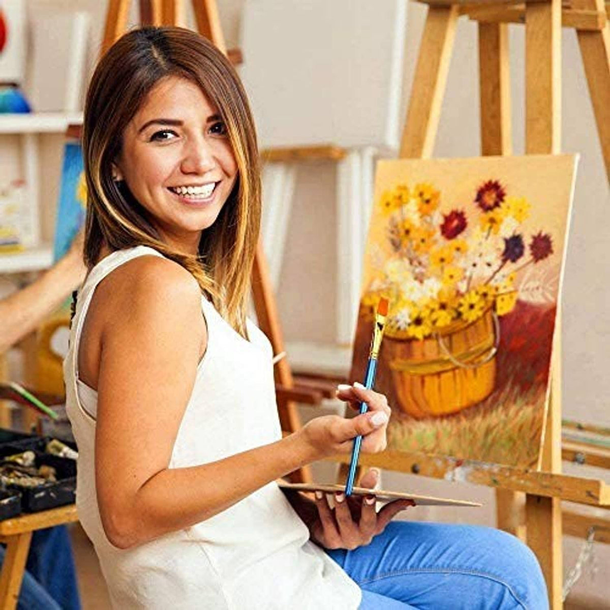 Paint brush with blue handle and gold ferrule in use, painting a small canvas