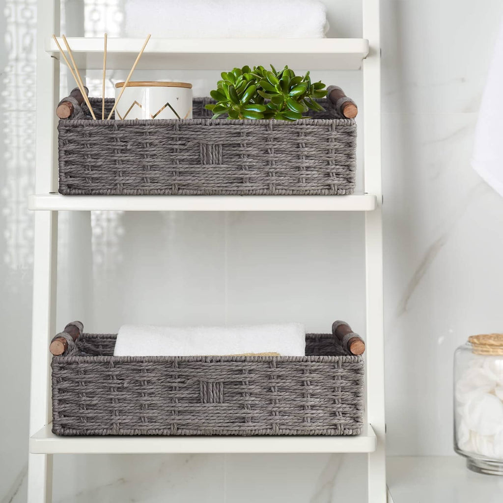 Grey woven storage basket set on white shelves, with rolled towels visible inside.