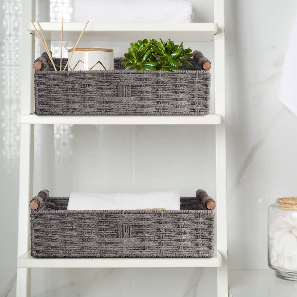 Grey woven storage basket set on white shelves, with rolled towels visible inside.